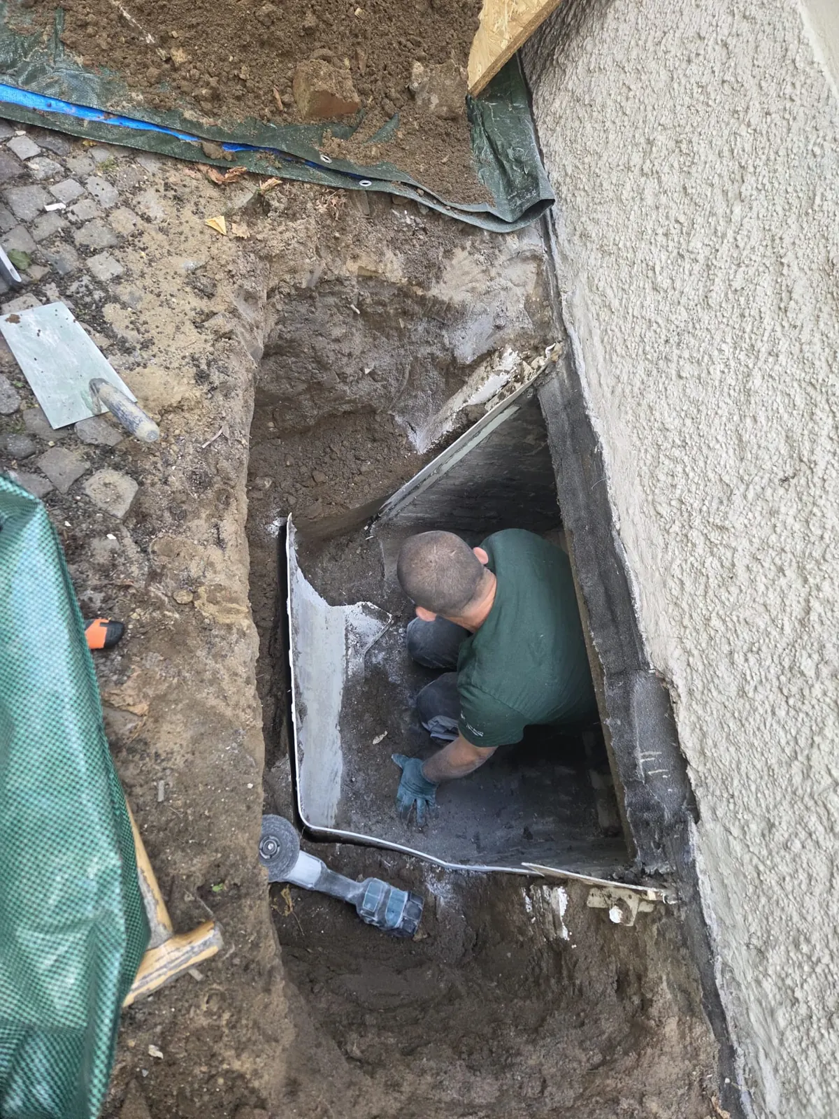 Offene Grube vor der Hauswand, Abdichtung und Ablauf für den neuen Lichtschacht werden vorbereitet