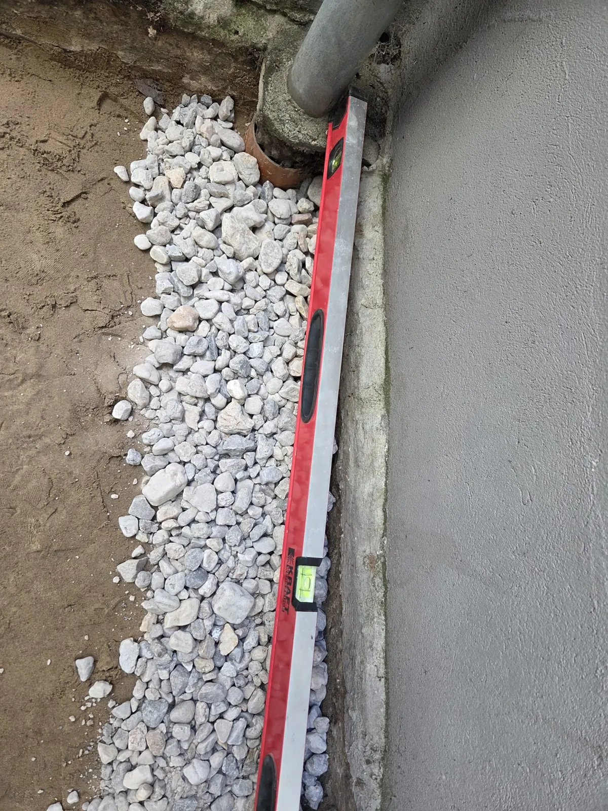 Traufstreifen aus Kies wird an der Hauswand mit der Wasserwaage angelegt